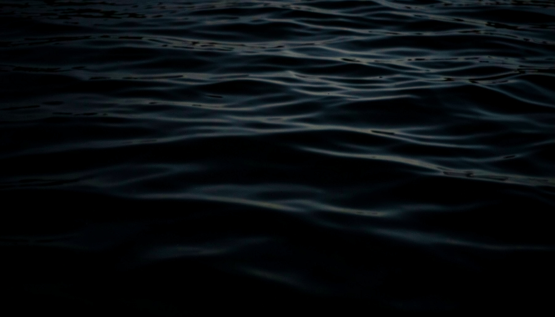 A dark, low-key photograph of calm deep water with soft ripples catching faint light, moody and contemplative.